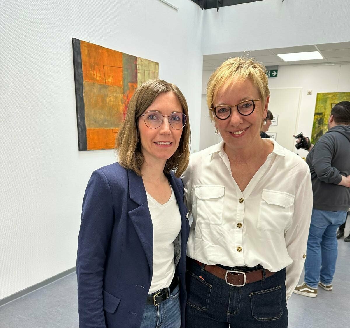 Die ausstellende Künstlerin Elisabeth Jux-Hiltrop und die Prokuristin der IBZ gGmbH Susanne Senge posieren für ein gemeinsames Portrait vor einem der Gemälde.